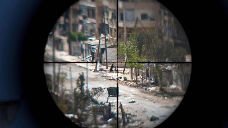 امرأة وطفلها يُشاهدان من خلال منظار بندقية قنص أحد مقاتلي المعارضة، أثناء فرارهما من حي سيف الدولة بمدينة إدلب شمال سوريا