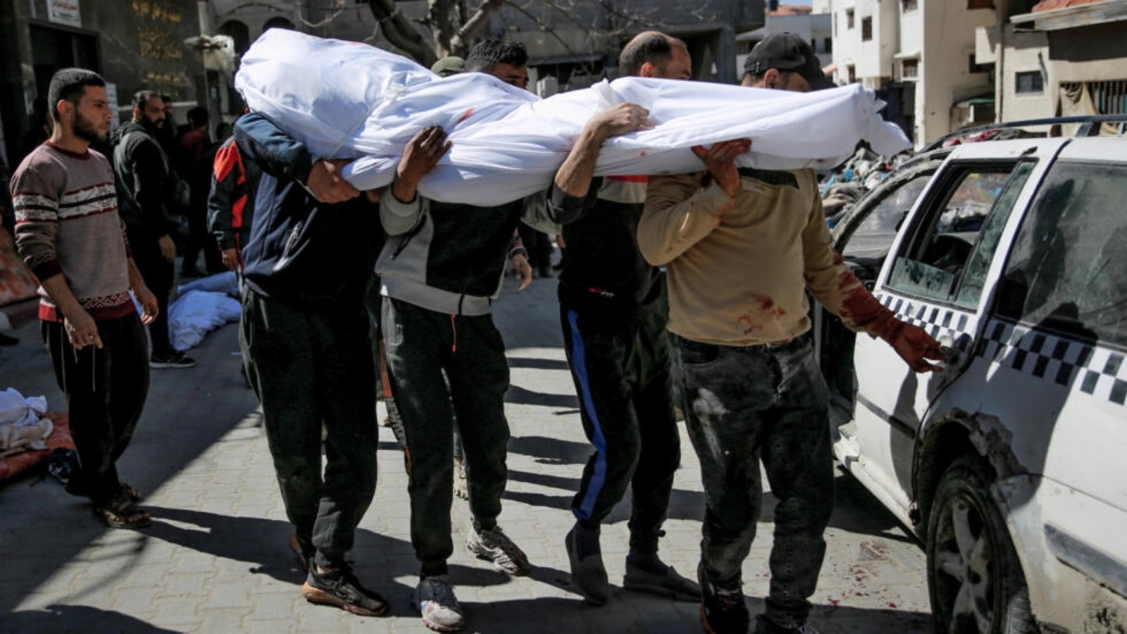 رجال يحملون جثة فلسطيني قُتل مع أكثر من مئة شخص خلال التدافع وعندما فتحت القوات الإسرائيلية النار على حشود اقتربت من شاحنات مساعدات عند نقطة توزيع في مدينة غزة في 29 شباط (فبراير) 2024 