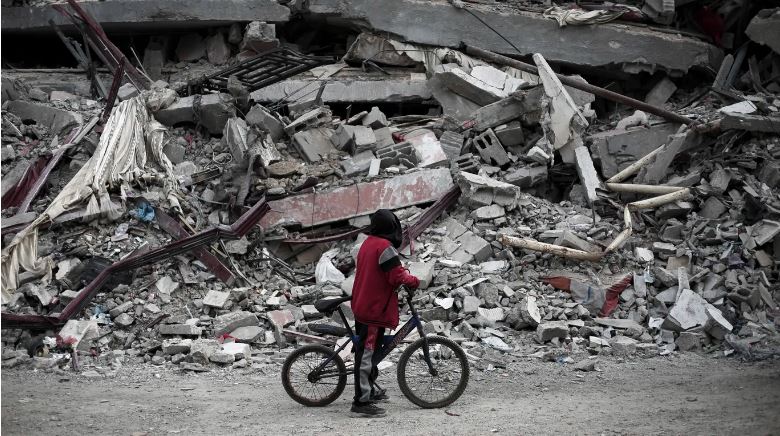 فلسطيني على متن دراجته ينظر إلى أنقاض منزل دمره القصف الإسرائيلي في رفح