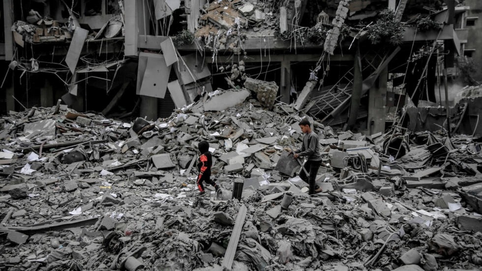 فلسطينيون يسيرون بين أنقاض البيوت التي دمرها القصف الإسرائيلي في مدينة غزة