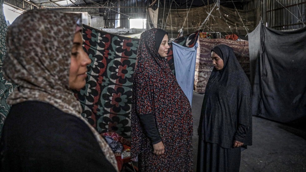 امرأة فلسطينية حامل (وسط) نازحة من شمال قطاع غزة تقف في مستودع لجأت إليه في مدينة رفح في جنوب القطاع في 29 شباط/فبراير 2024