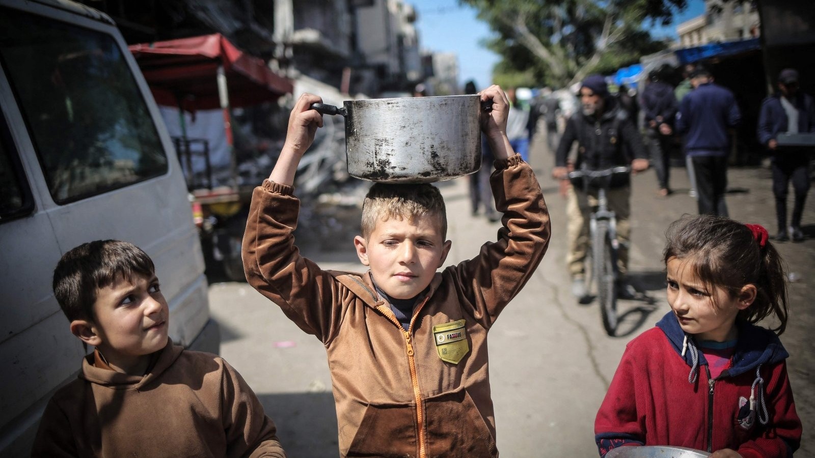 أطفال فلسطينيون يحملون أدوات المطبخ أثناء سيرهم نحو نقطة توزيع المواد الغذائية في خان يونس، قطاع غزة، فلسطين، 7 مارس، 2024