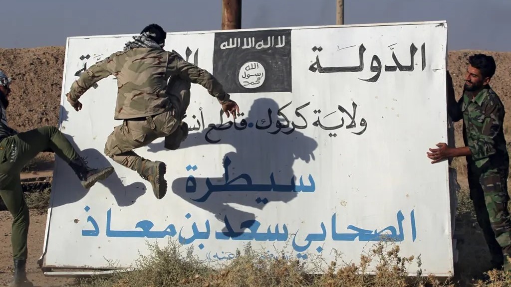 مقاتلون من الحشد الشعبي، الذين يدعمون القوات العراقية، يركلون لوحة تحمل شعار تنظيم الدولة الإسلامية “داعش” في الحويجة، في 6 أكتوبر 2017