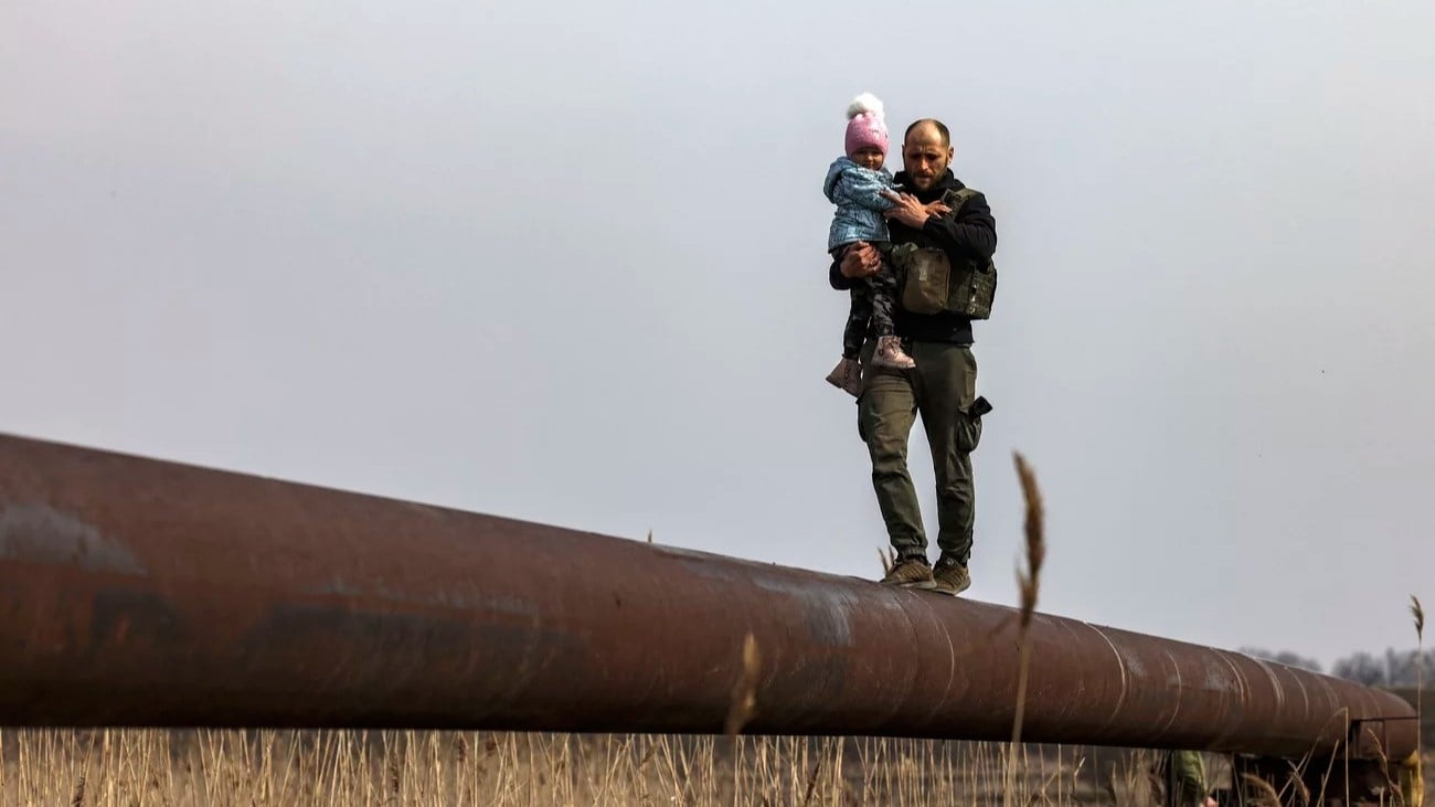 جندي غير أوكراني يحمل طفل عائلة نازحة للمساعدة في عبور النهر، على مشارف كييف