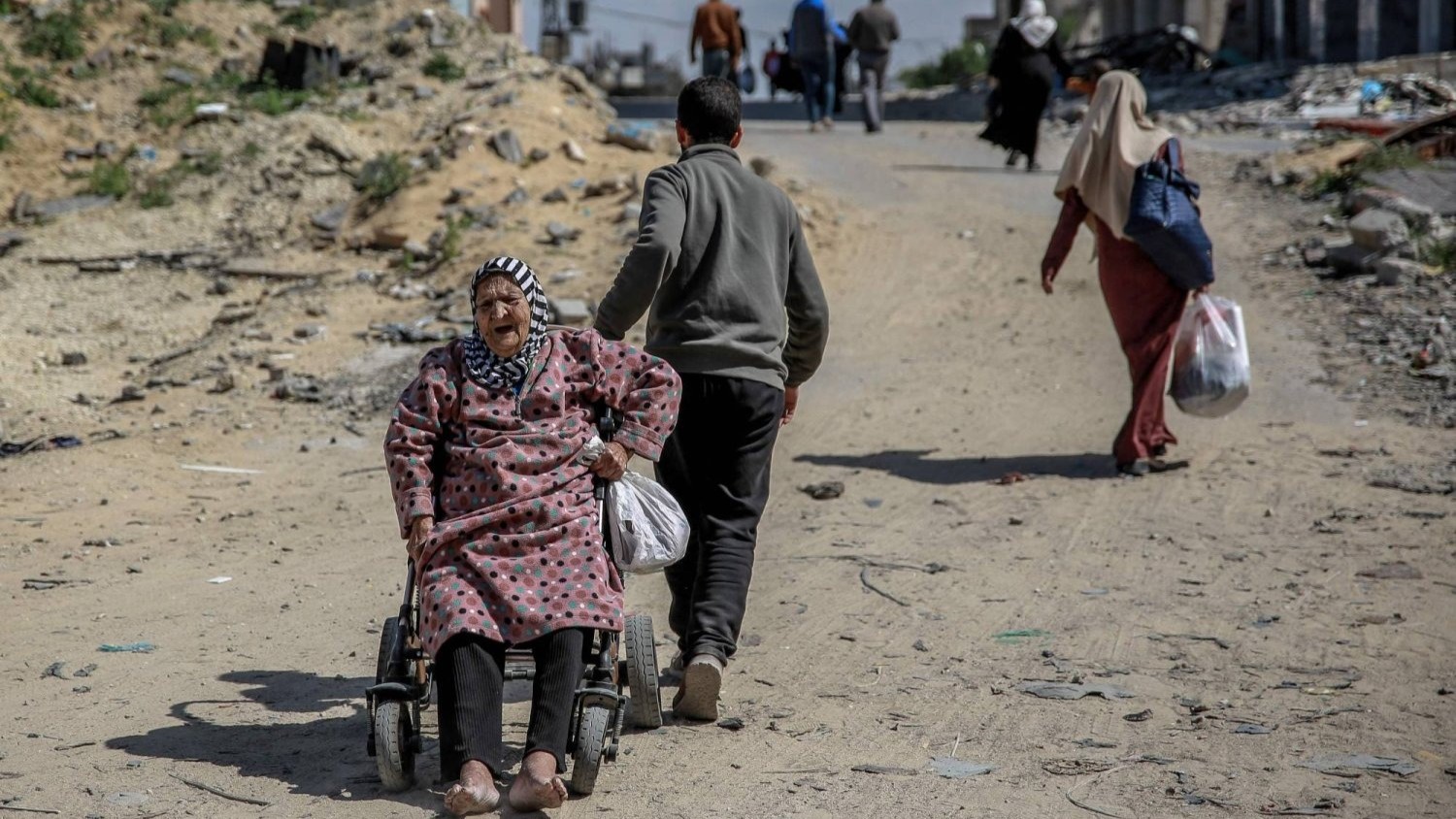 رجل يسحب امرأة فلسطينية مسنة على كرسي متحرك أثناء نزوح العائلات في غزة
