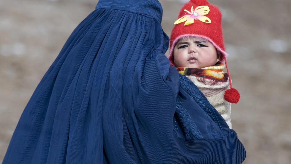امرأة أفغانية ترتدي البرقع تحمل طفلاً إلى مركز صحي لتطعيمه في اطار برنامج 