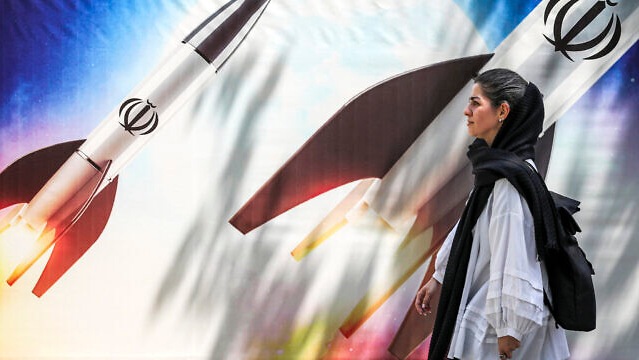 امرأة تمر من أمام لافتة تستعرض إطلاق صواريخ عليها شعار الجمهورية الإسلامية الإيرانية في وسط طهران في 15 أبريل 2024