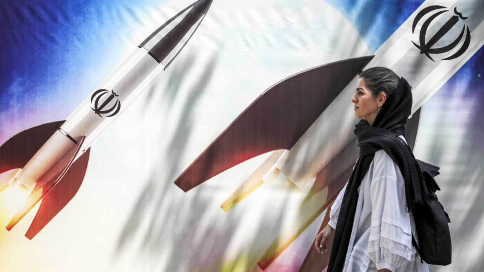 امرأة تمر أمام ملصق يصور إطلاق صواريخ تحمل شعار جمهورية إيران الإسلامية في وسط طهران في 15 نيسان (أبريل) 2024 
