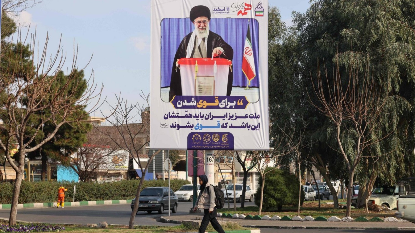  امرأة تمر أمام لوحة إعلانية للحملة الانتخابية تحمل صورة المرشد علي خامنئي بمدينة قم الإيرانية 