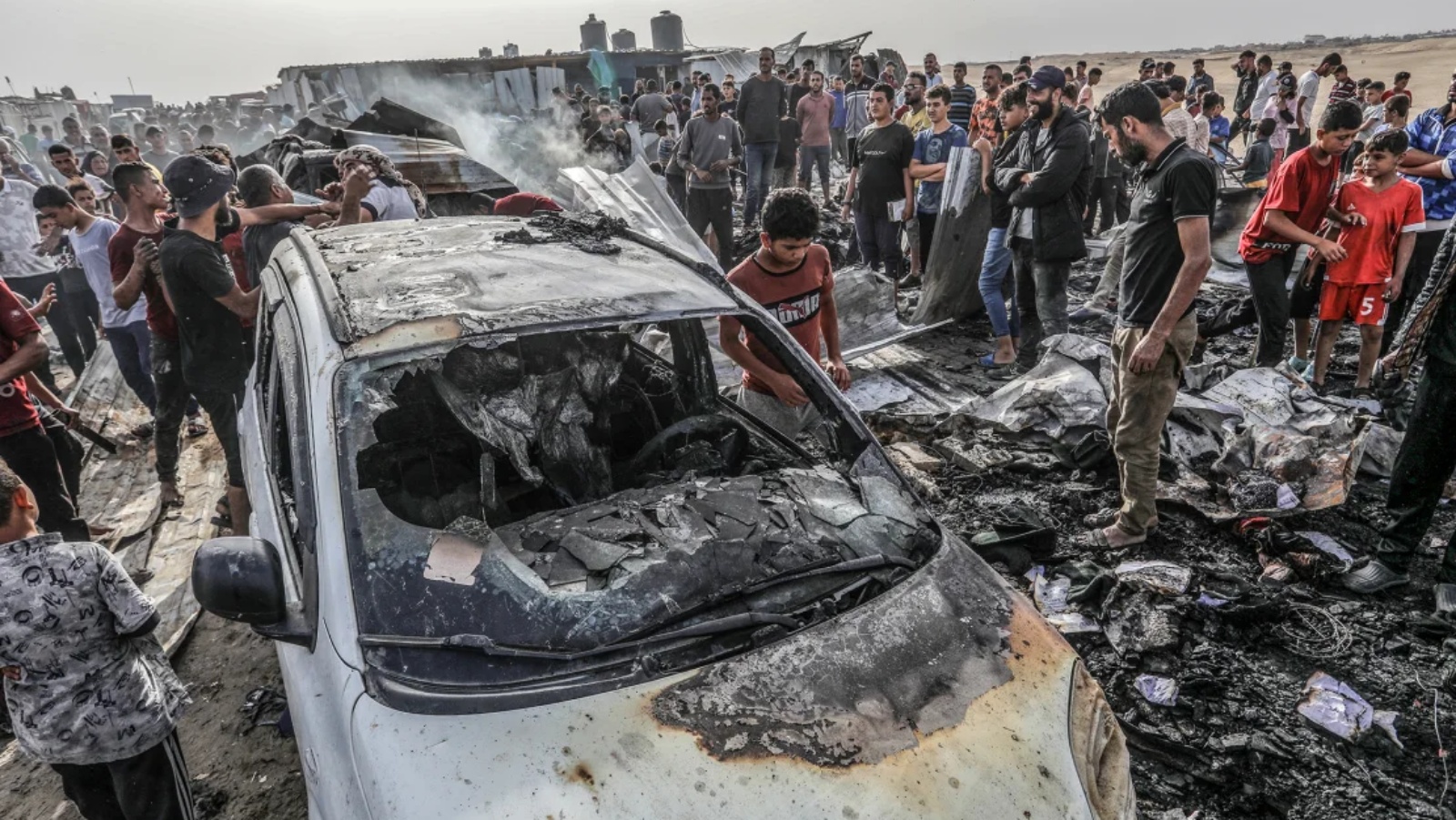 فلسطينيون يتجمعون حول سيارة محترقة بعد غارة جوية إسرائيلية على مخيم في مدينة رفح جنوب قطاع غزة يوم الاثنين