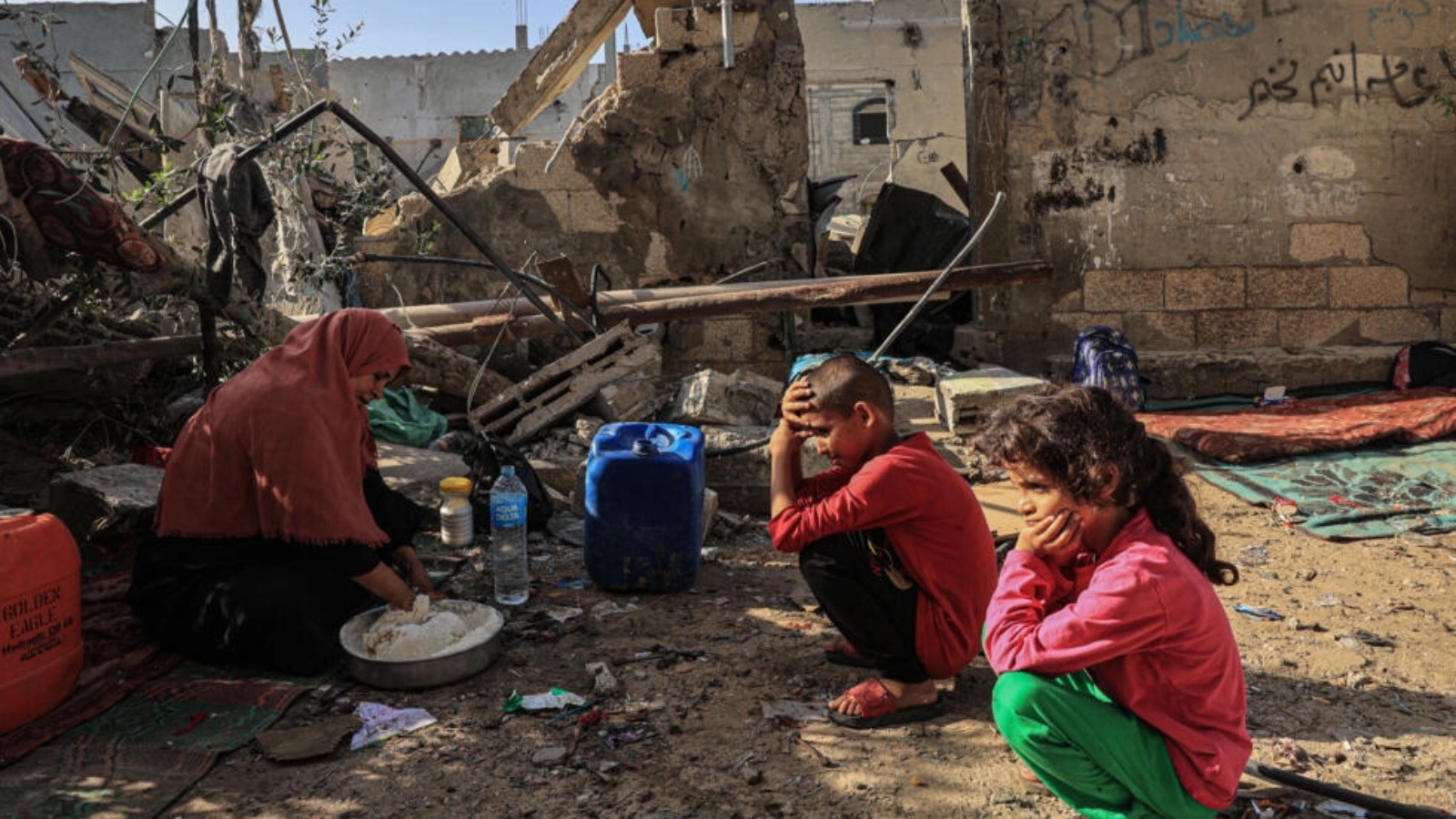 امرأة تعجن الخبز أمام أحفادها وسط أنقاض منزل دمر بغارة إسرائيلية في رفح