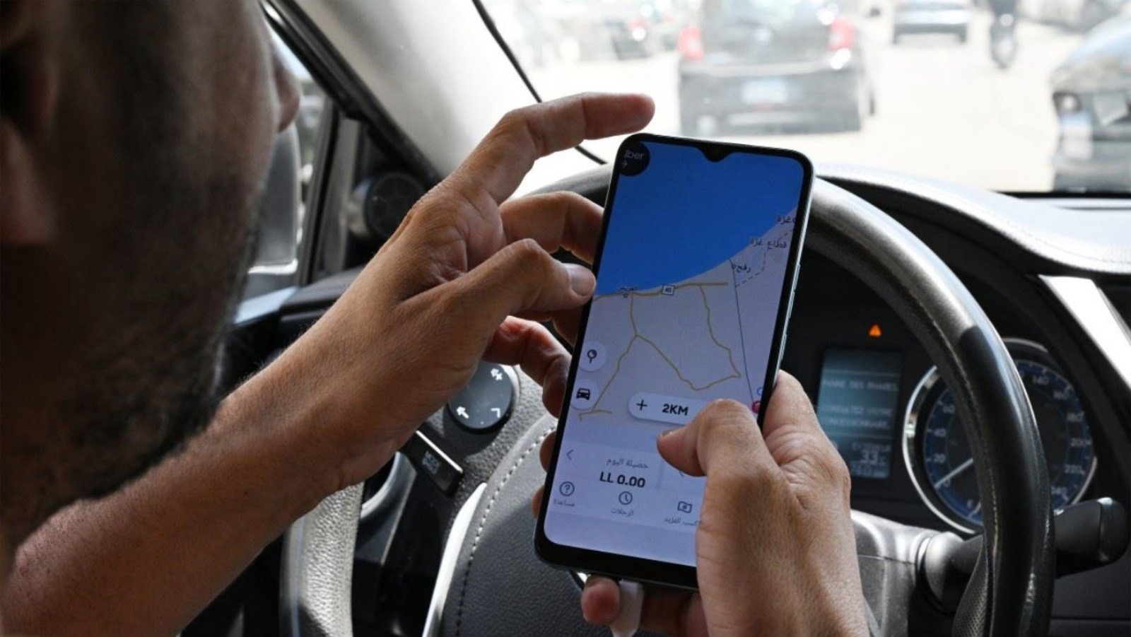 السائق اللبناني حسين خليل ينظر إلى نظام تحديد المواقع العالمي (GPS) على تطبيق أوبر الذي يُظهر أنه في منطقة الهرمل في وادي البقاع الشرقي بلبنان، بينما يجلس في سيارته في شارع الحمرا ببيروت في 11 حزيران (يونيو) 2024 