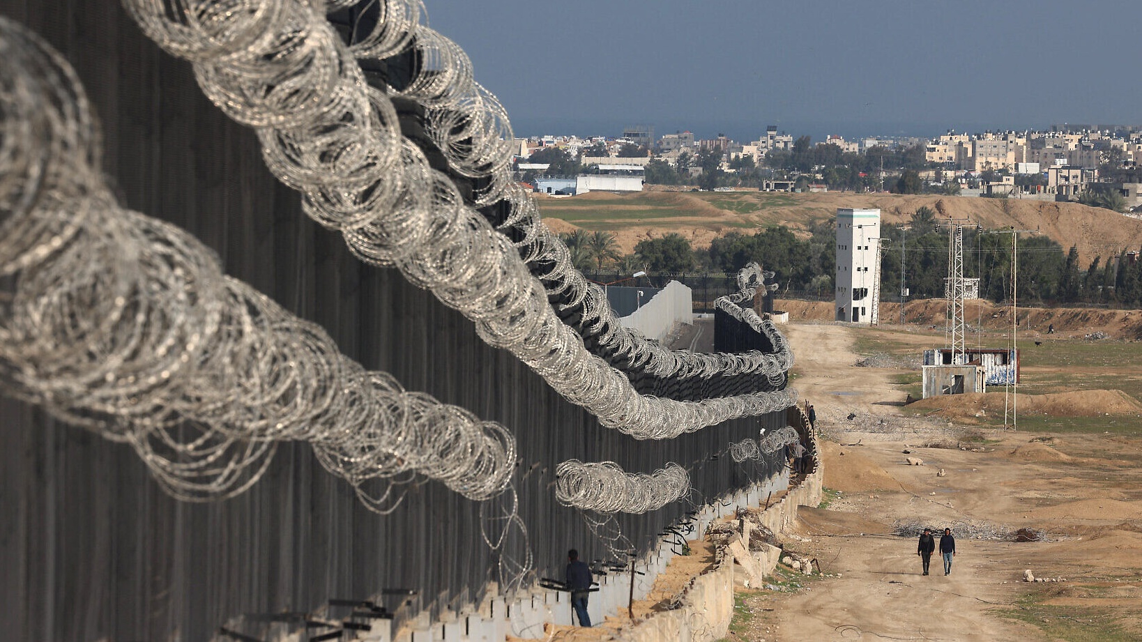 نازحون فلسطينيون يسيرون بجوار السياج الحدودي بين غزة ومصر في رفح (أ.ف.ب)