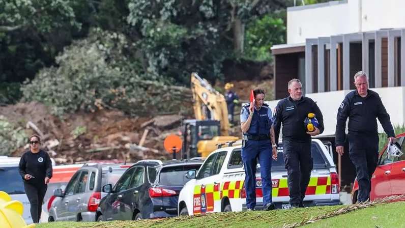 رجال شرطة ومسؤولون يسيرون في جبل مونغانوي بمدينة تاورانجا، حيث تسببت الأمطار في انهيار أرضي، بينما تواصل فرق الإنقاذ المحلية عمليات البحث عن المفقودين، في 22 يناير/كانون الثاني عام 2026 -