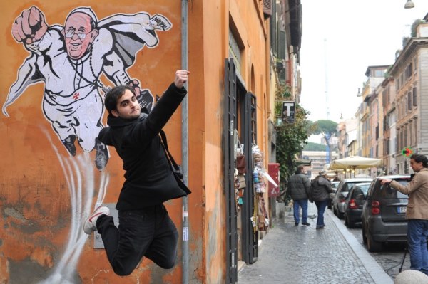 سائح يقفز أمام اللوحة الجدارية التي تصور البابا على هيئة سوبرمان