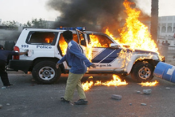 متظاهر بحريني معارض أمام سيارة شرطة تحترق