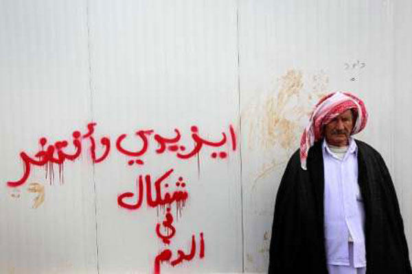عراقي إيزيدي يقف في مخيم في دهوك امام جدار كتب عليه 