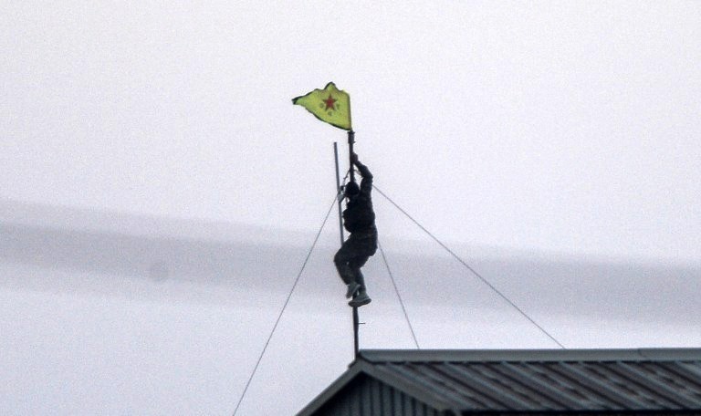 مقاتل كردي يرفع علم الأكراد فوق مبنى في مدينة تل ابيض السورية