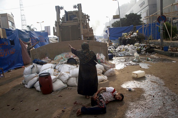 سيدة تقف أمام جرافة وبجانبها مصاب في ساحة رابعة
