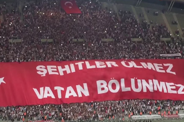 الجمهور التركي رفع علم كبير كتب عليه باللغة التركية : ( الشهداء لا يموتون بل هم خالدو