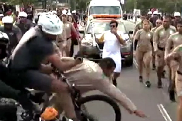 الفيديو يظهر شرطيا على دراجة نارية يصطدم باخر على دراجة هوائية مباشرة امام حامل الشعلة الاولمبية