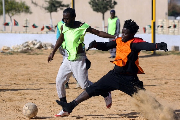مهاجران كاميروني بالبرتقالي وسنغالي بالاصفر خلال مباراة كرة القدم في مركز احتجاز تاجوراء في طرابلس