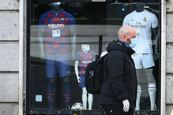 رجل يرتدي قناعا طبيا واقيا يمر بجانب متجر للألبسة الرياضية في مدريد في 17 آذار/مارس 2020.