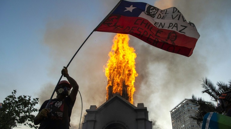 متظاهر يلوح بعلم تشيلي أمام كنيسة الصعود التي تحترق في سانتياغو في 18 أكتوبر 2020