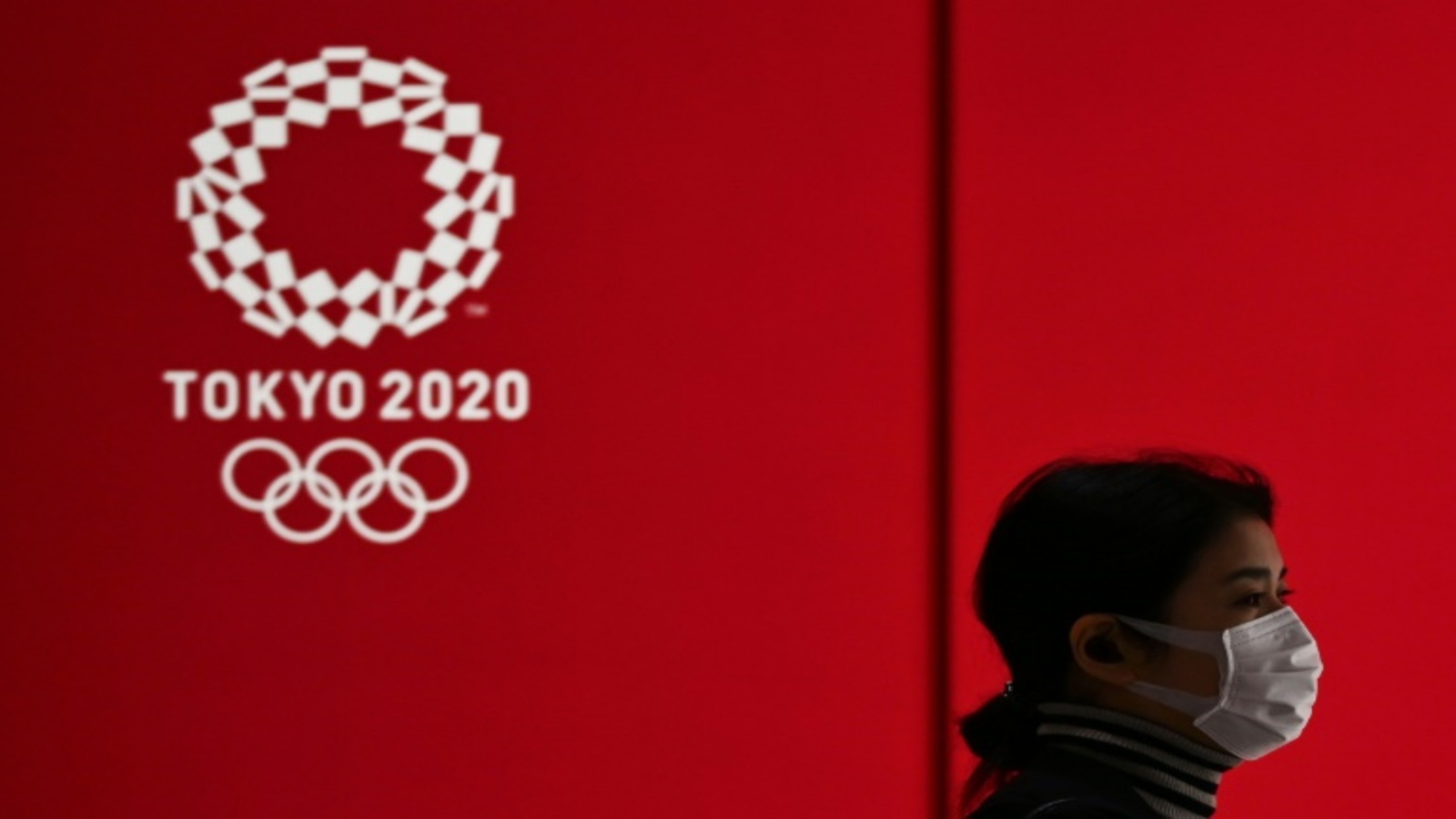 امرأة تضع كمامة لدى مرورها أمام شعار الألعاب الأولمبية في طوكيو في 24 آذار/مارس 2020