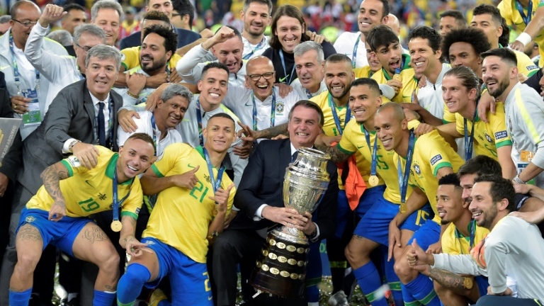 الرئيس البرازيلي جايير بولسونارو يحمل كأس كوبا أميركا وسط لاعبي منتخب بلاده عقب التتويج باللقب في السابع من تموز/يوليو 2019.
