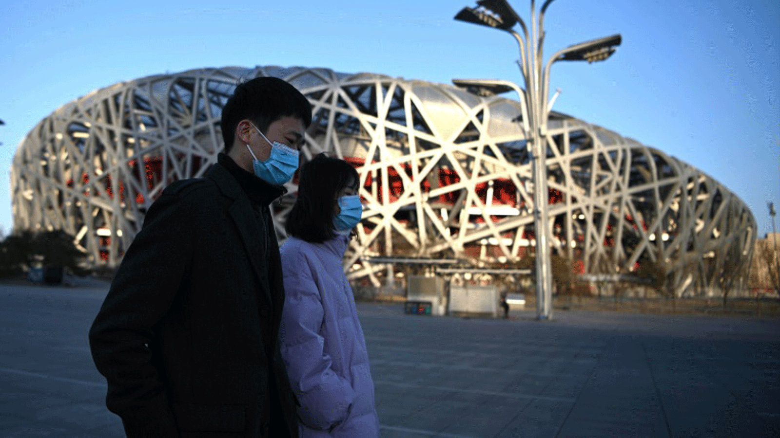 صينيان يمران أمام ملعب اولمبياد بكين الشتوي