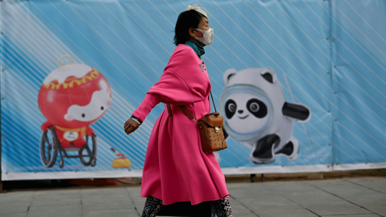 امرأة تمر أمام لافتة عليها تعويذات أولمبياد بكين. 5 كانون الأول/ديسمبر 2021