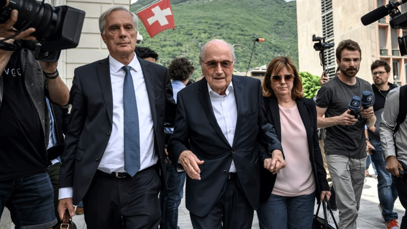رئيس الاتحاد الدولي لكرة القدم السابق السويسري جوزيف بلاتر (في الوسط) برفقة ابنته كورين ومحاميه لورنز إرني في نهاية اليوم الاول من محاكمته بتهمة الاحتيال في سويسرا في مدينة بيلينتسونا. 8 حزيران/يونيو 2022