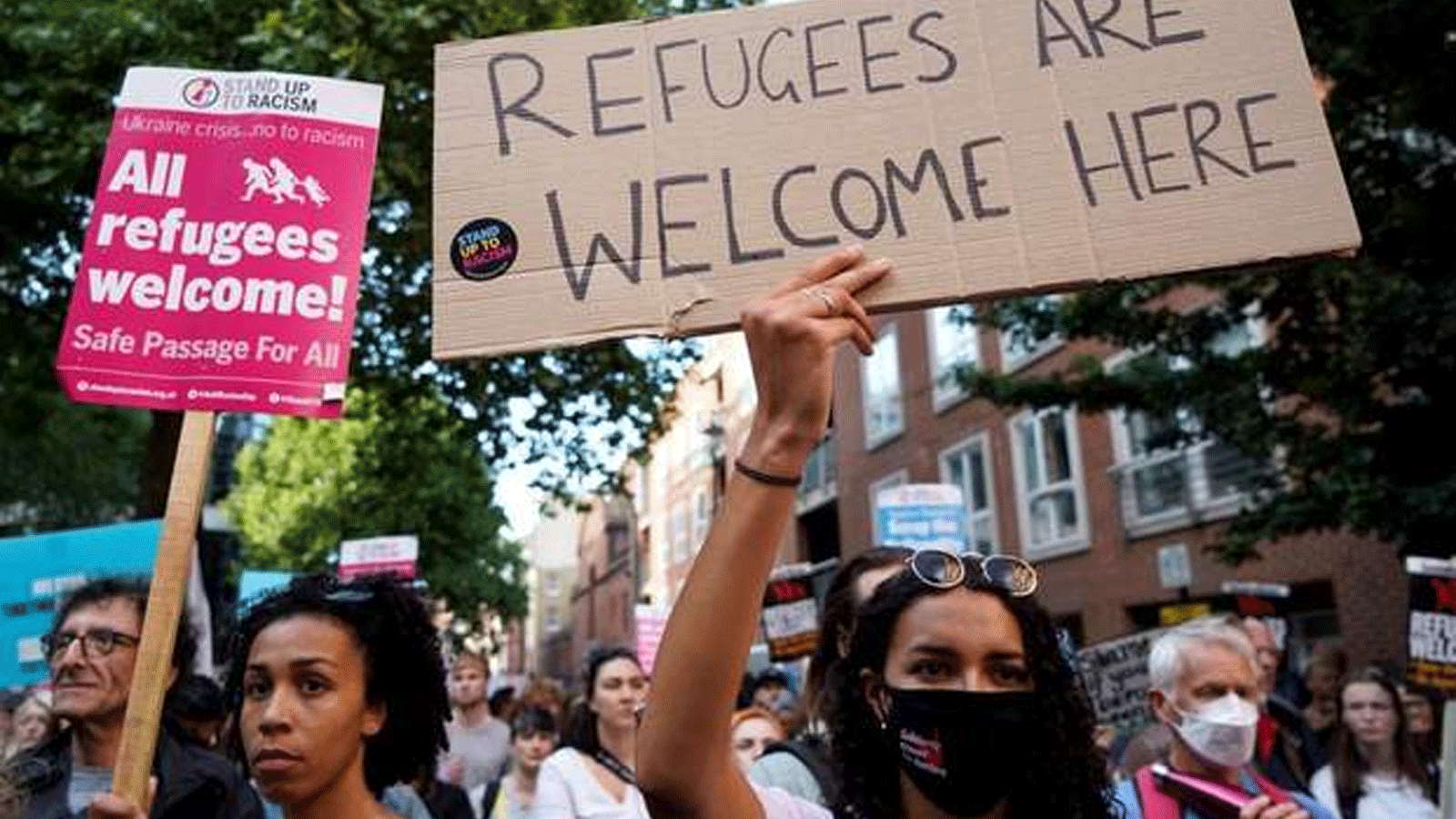 صورة أرشيفية لمتظاهرين في بريطانيا يحملون لافتات تُرحب بطالبي اللجوء