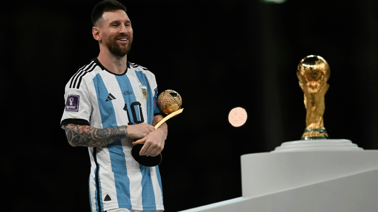 ليونيل ميسي يقف أمام كأس العالم FIFA بعد فوز الأرجنتين على فرنسا بركلات الترجيح في النهائي