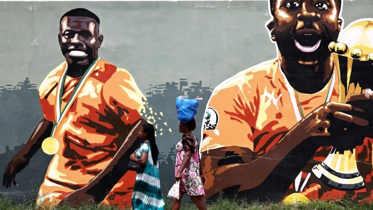 نساء يمرنّ مقابل جدارية لنجوم ساحل العاج المتوجين بكأس أمم إفريقيا 2015 في أبيدجان في 20 كانون الثاني/يناير 2024 خلال كأس أمم إفريقيا