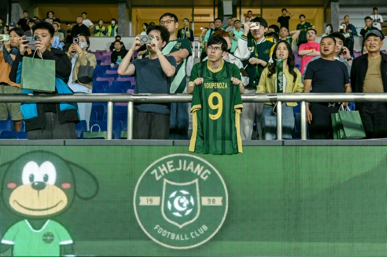 مشجعٌ لفريق تشجيانغ الصيني رفع قميص مهاجمه الدولي الغابوني آرون بوبيندزا الذي عُثر عليه ميتًا إثر سقوطه من الطابق الحادي عشر في مبنى في هانغجو في 16 نيسان/أبريل 2025