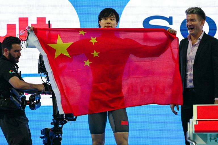 الصيني تشين هايانغ يحمل علم بلاده بعد فوزه سباق 100 م صدرا في بطولة العالم للسباحة. سنغافورة، في 28 تموز/يوليو 2025