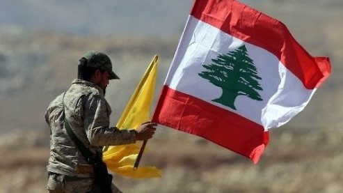 عضو في حزب الله يحمل العلم اللبناني وعلم حزبه خلال جولة صحفية قرب الحدود