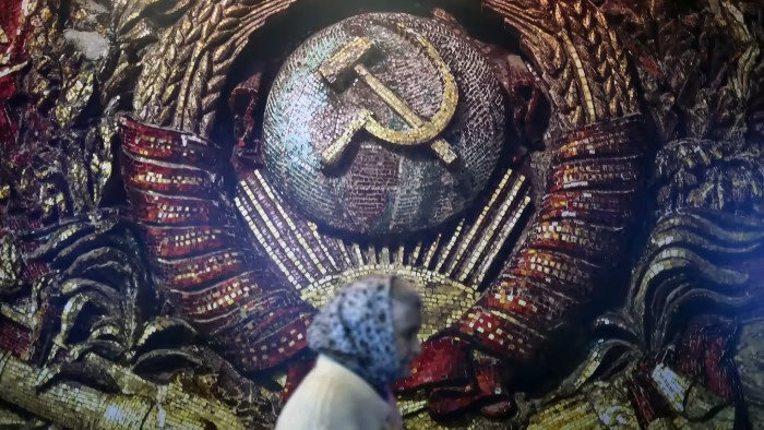صورة من الأرشيف لروسية تمر بجانب شعار الحزب الشيوعي السوفياتي محفورًا في جدار أحد شوارع موسكو