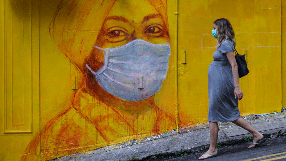 حامل تمر بالقرب من جدارية لامرأة ترتدي كمامة في هونغ كونغ
