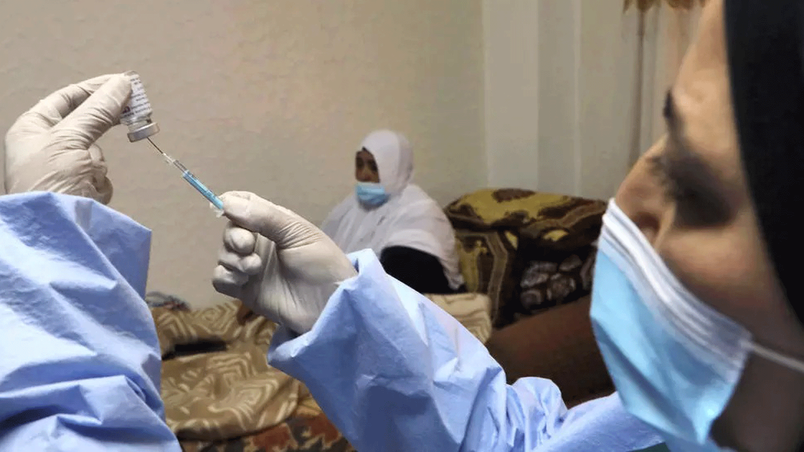 لقطة لممرضة تُجهز اللقاح لسيدة مسنة في الضفة الغربية
