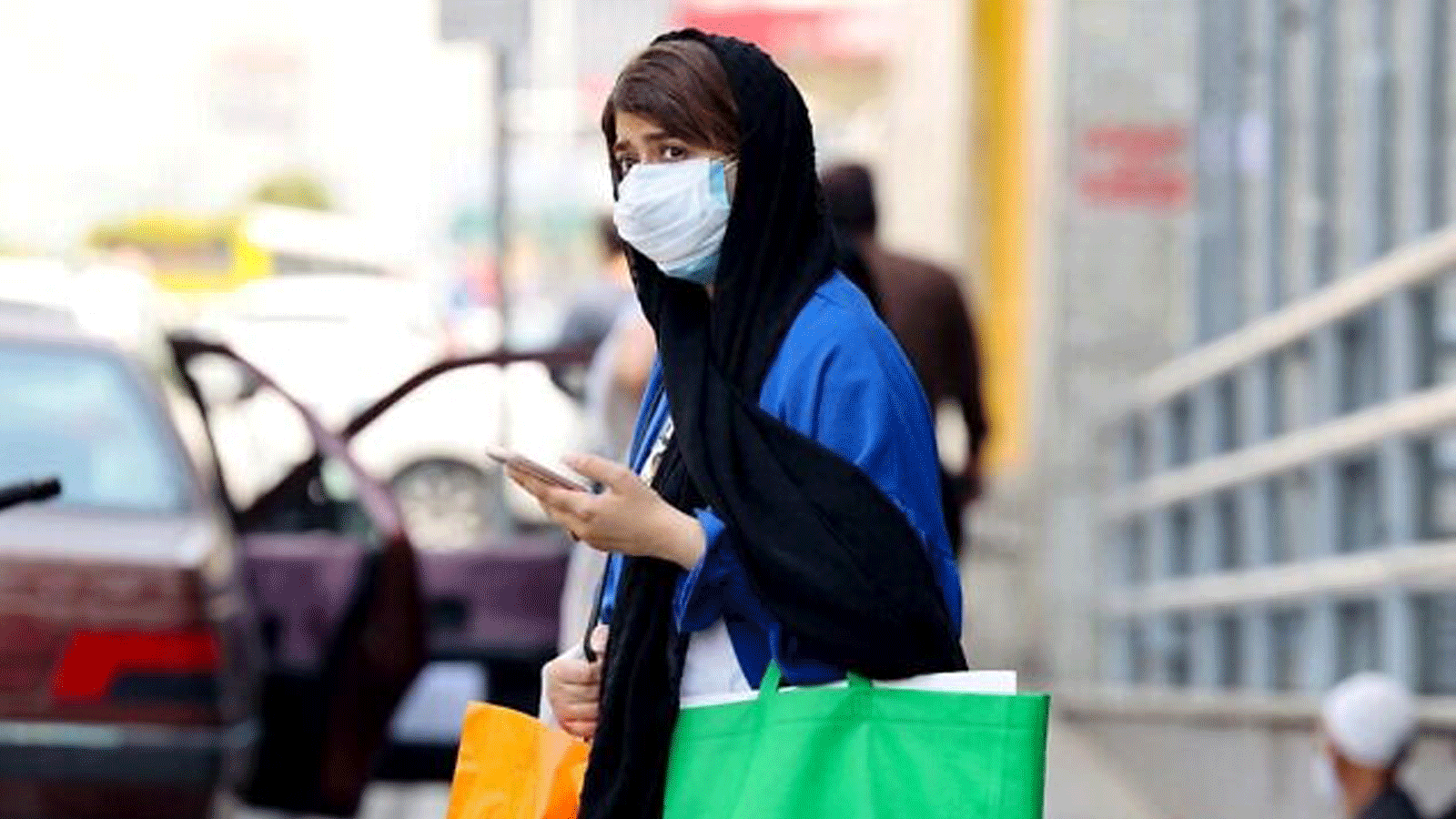 امرأة إيرانية ترتدي قناع الوجه في انتظار عبور أحد شوارع العاصمة طهران، في 3 تموز/ يوليو 2021