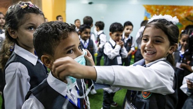 فتاة تضع قناعًا على وجه صبي خلال جلسة توعية حول مرض فيروس كورونا في غزة