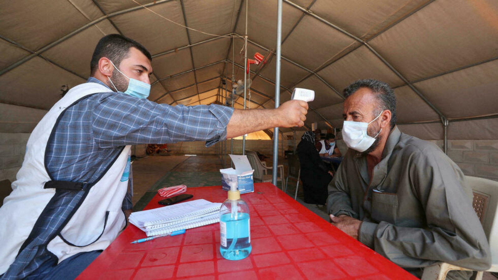 عامل صحي يقيس حرارة رجل في إحدى المراكز المخصصة لكورونا في إدلب، سوريا.