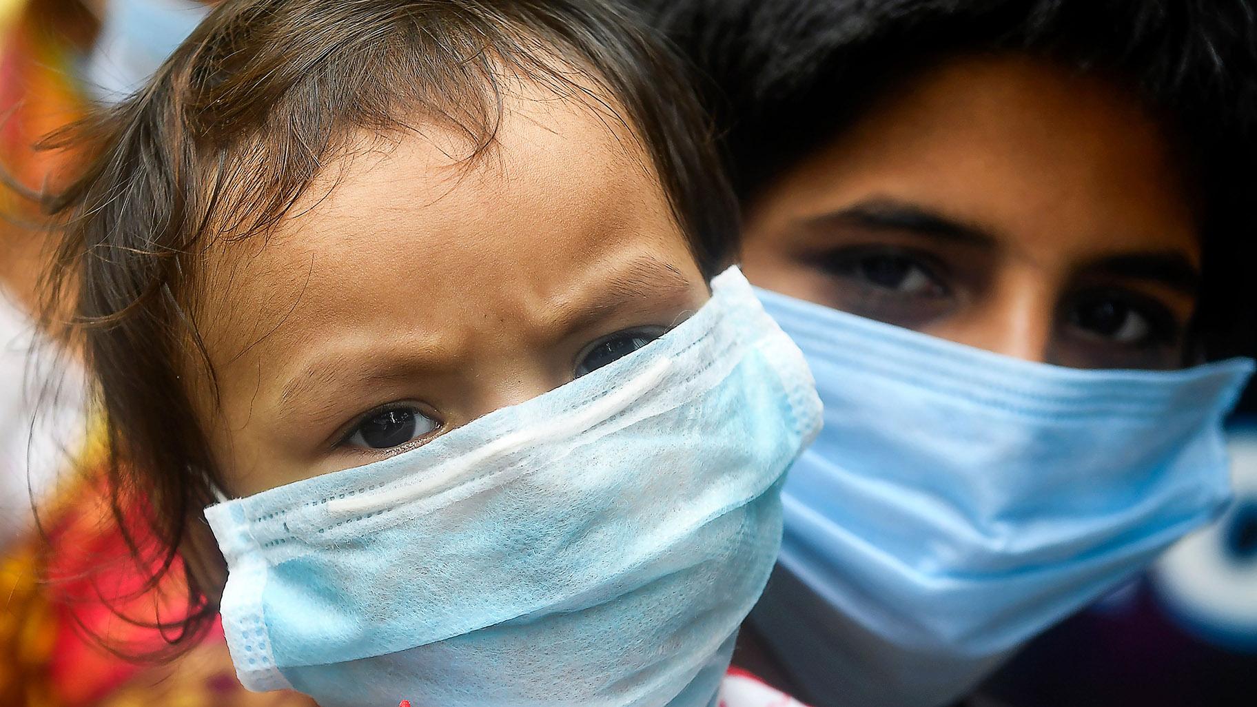طفلان يرتديان قناعين للوجه ينتظران في طابور مع آخرين لأخذ عينات مسحة لاختبار فيروس كورونا في كولكاتا في 28 يوليو 2020.