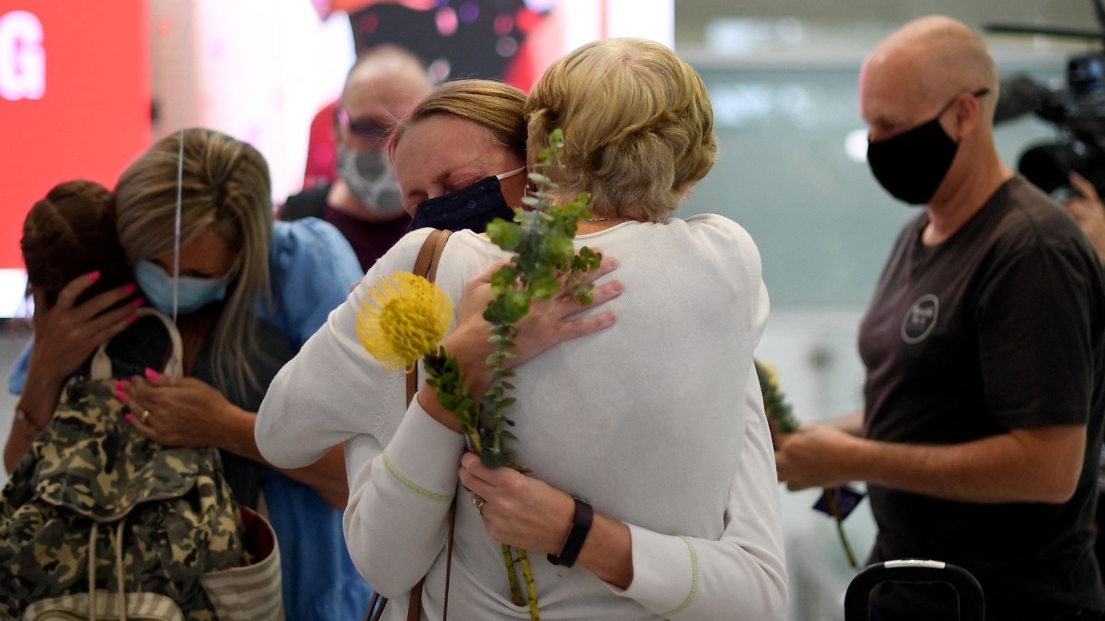 أفراد أسرة يحتفلون بلمّ شملهم عند وصولهم إلى مطار سيدني الدولي في 1 تشرين الثاني/نوفمبر 2021، حيث أعيد فتح الحدود الدولية لأستراليا بعد 600 يوم تقريبًا من بدء الإغلاق الوبائي.