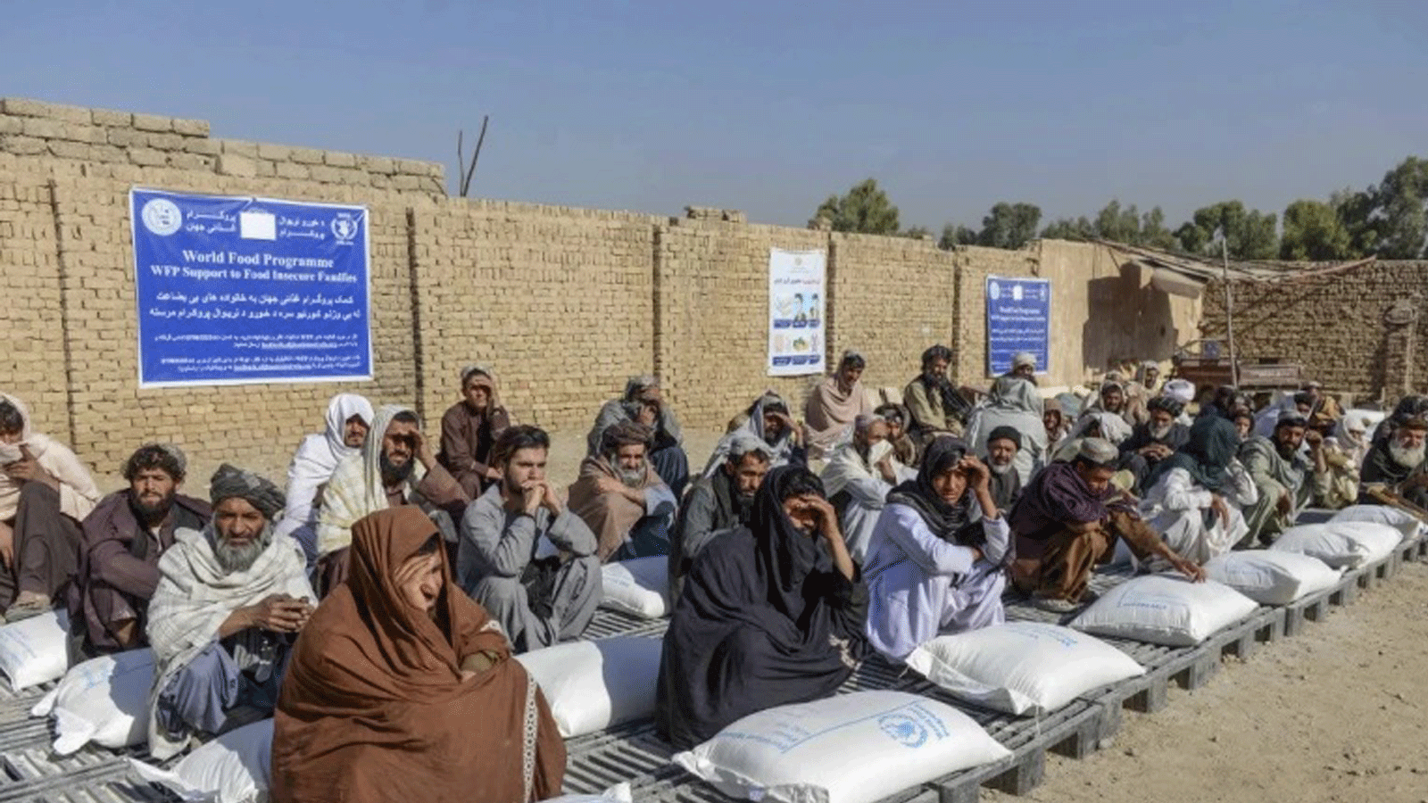 الأفغان يجلسون بجانب أكياس المساعدات الغذائية التي وزعها برنامج الأغذية العالمي في قندهار