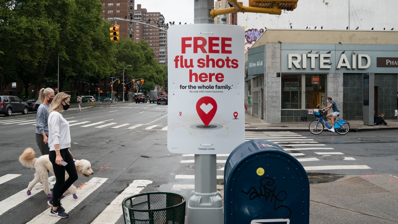 أشخاص يمرون أمام إعلان مجاني للقاح الأنفلونزا خارج صيدلية في نيويورك في أغسطس 2020