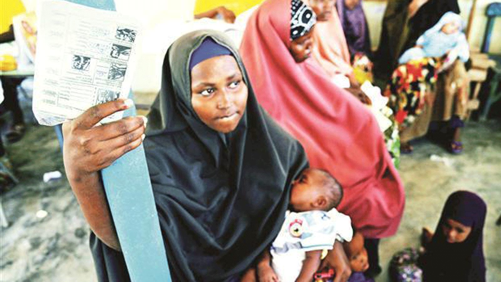 صورة لأم صومالية، تحمل بطاقة طبية، تنتظر إعطاء طفلها حقنة لقاح خماسي التكافؤ. 